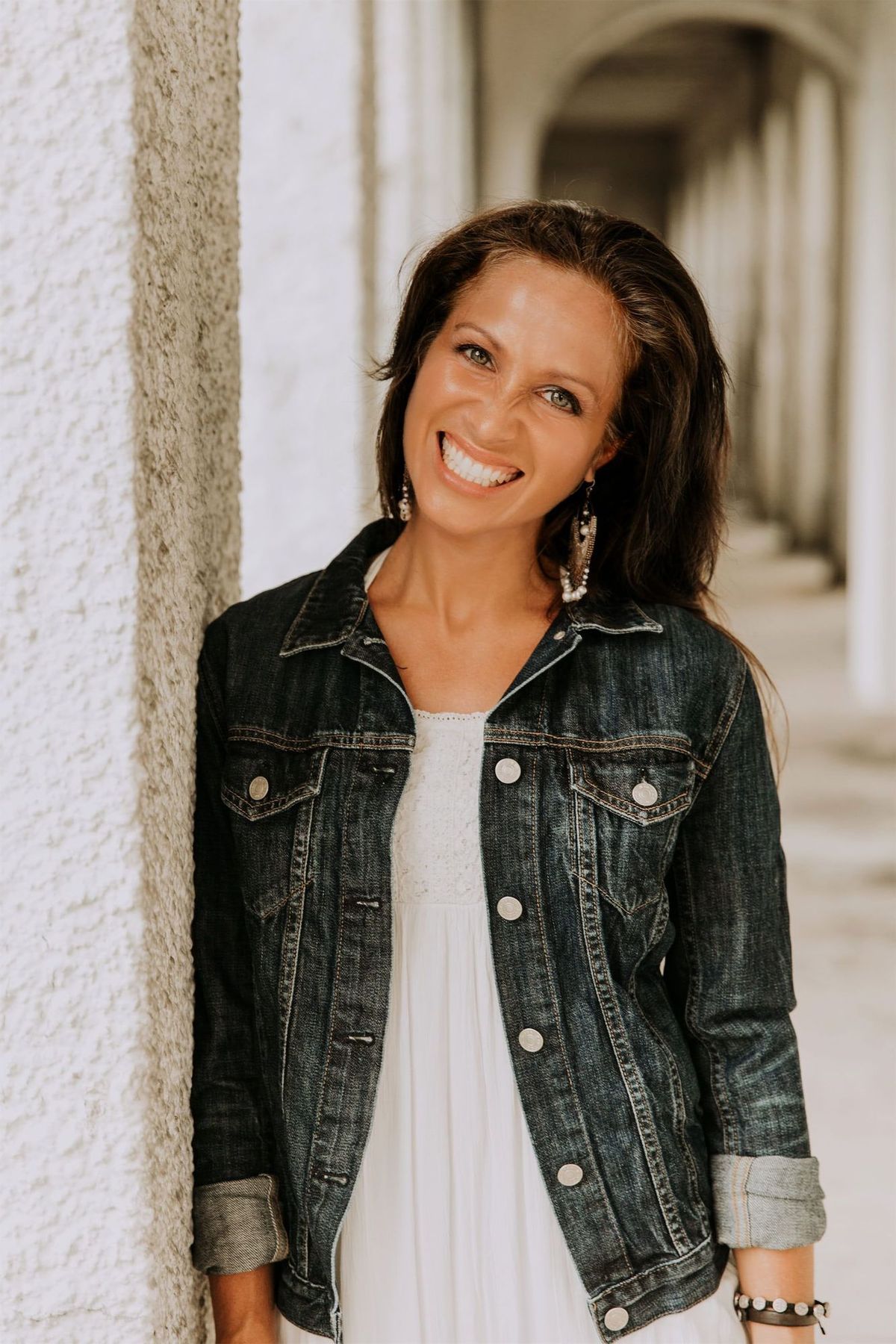 Maria Spears in a white shirt and jean jacket headshot by a white pillar version three