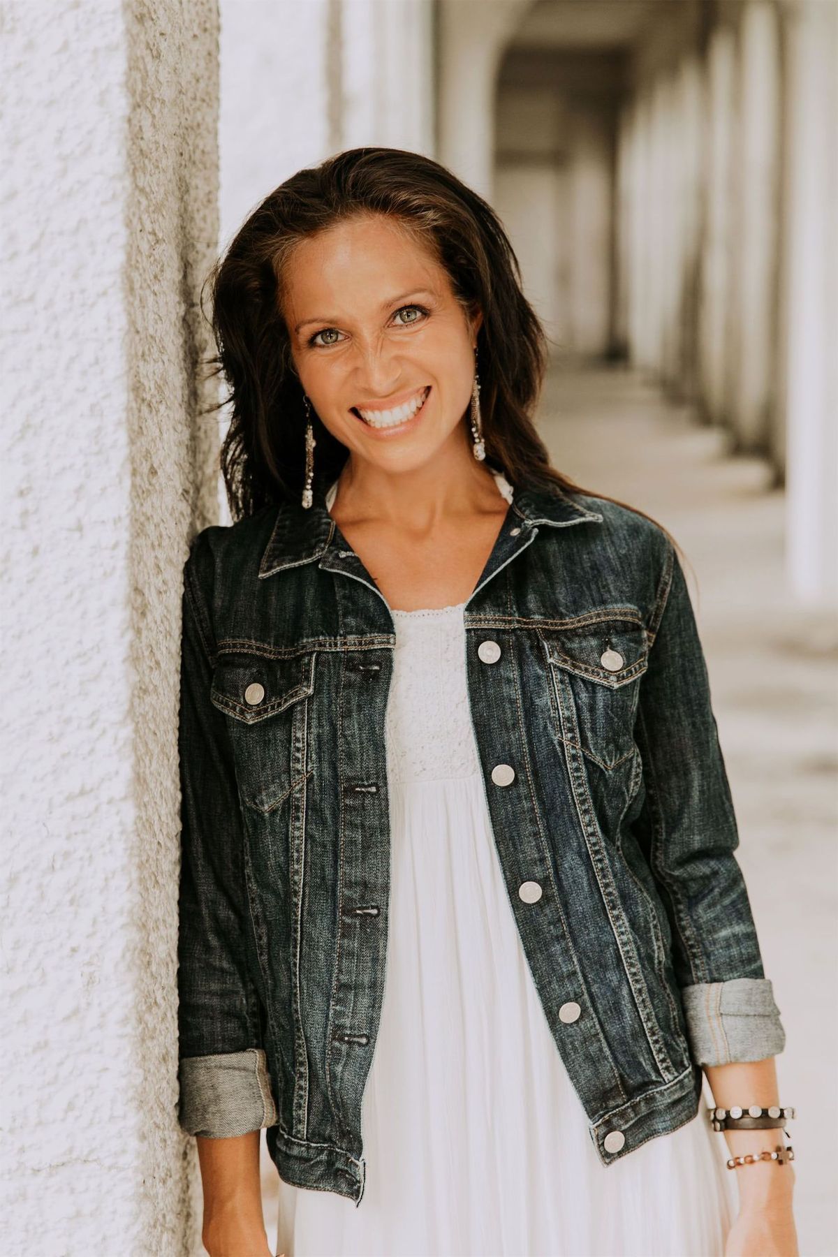 Maria Spears in a white shirt and jean jacket headshot by a white pillar version one
