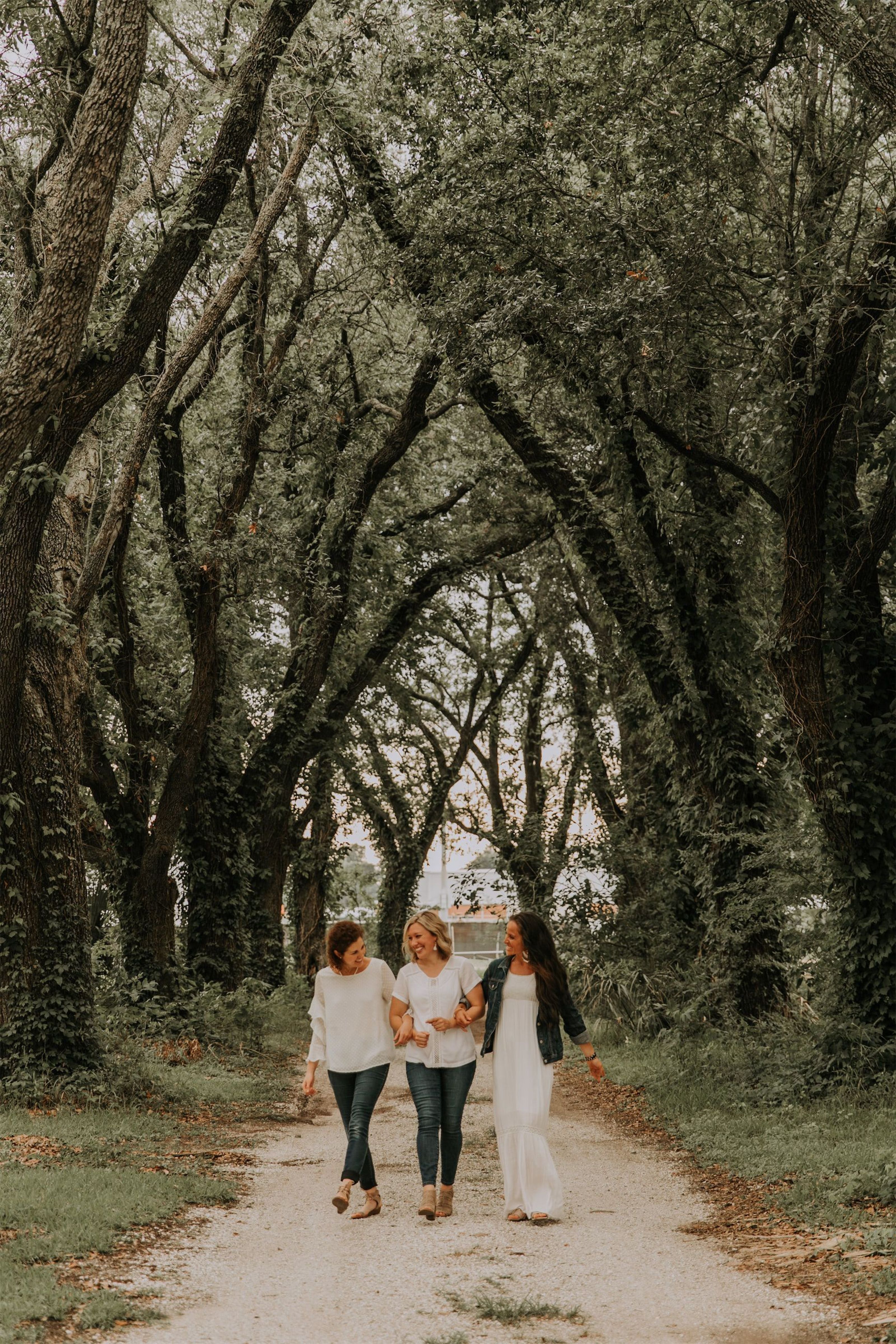 Kara Klein Oubre, Christine Simpson Wessa, and Maria Spears on a path near trees walking towards the camera arm in arm