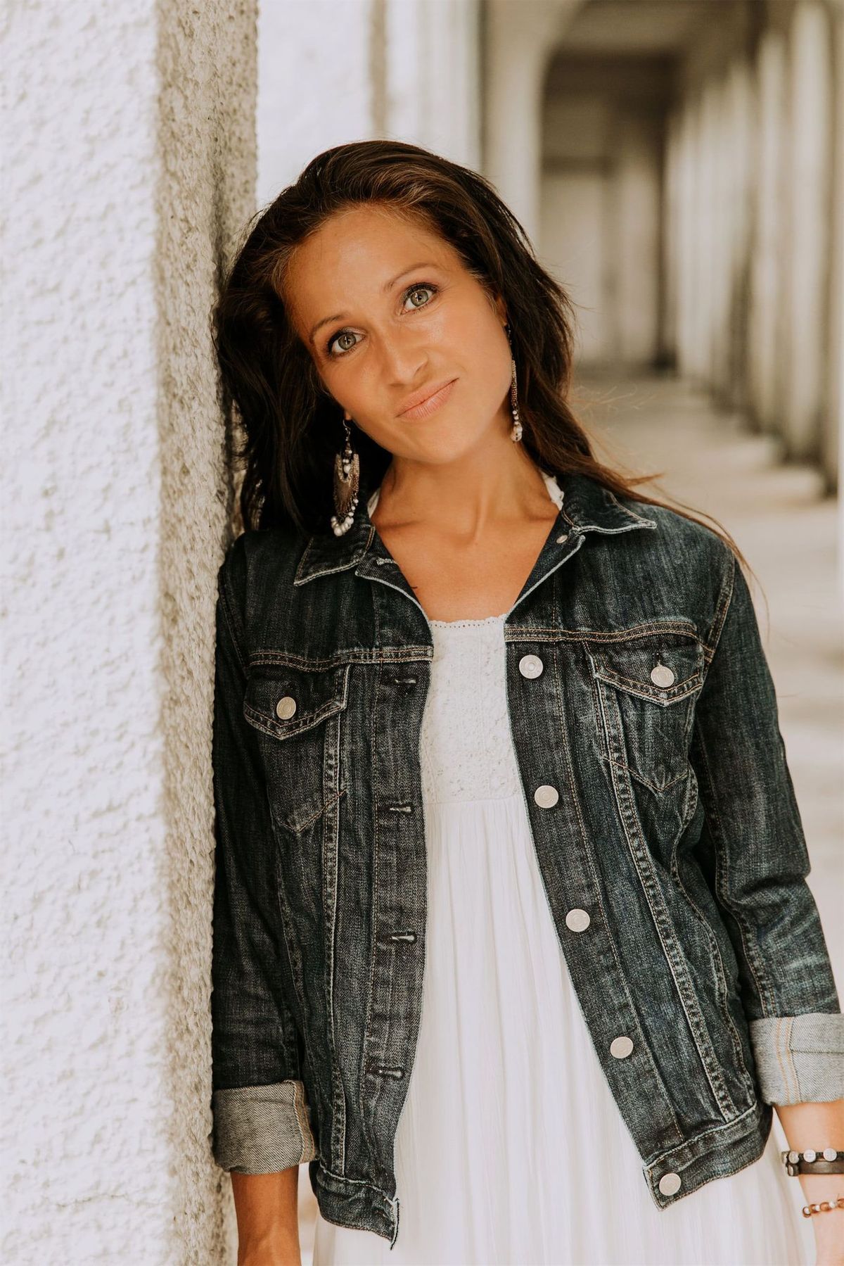 Maria Spears in a white shirt and jean jacket headshot by a white pillar version two