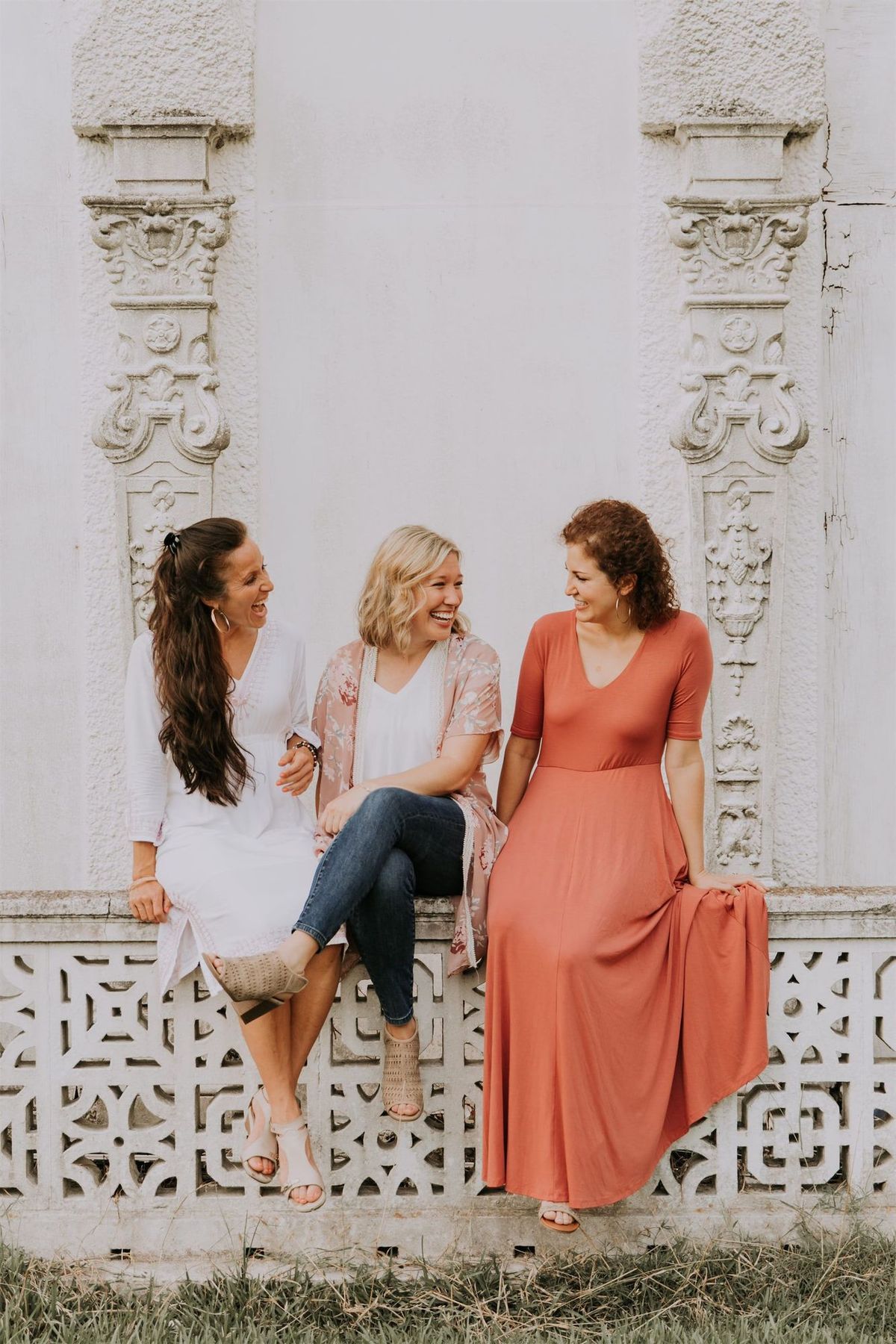 Kara Klein Oubre in a red dress, Christine Simpson Wessa in a flower shirt, and Maria Spears in a dress sitting on a stone wall vertical orientation version eight