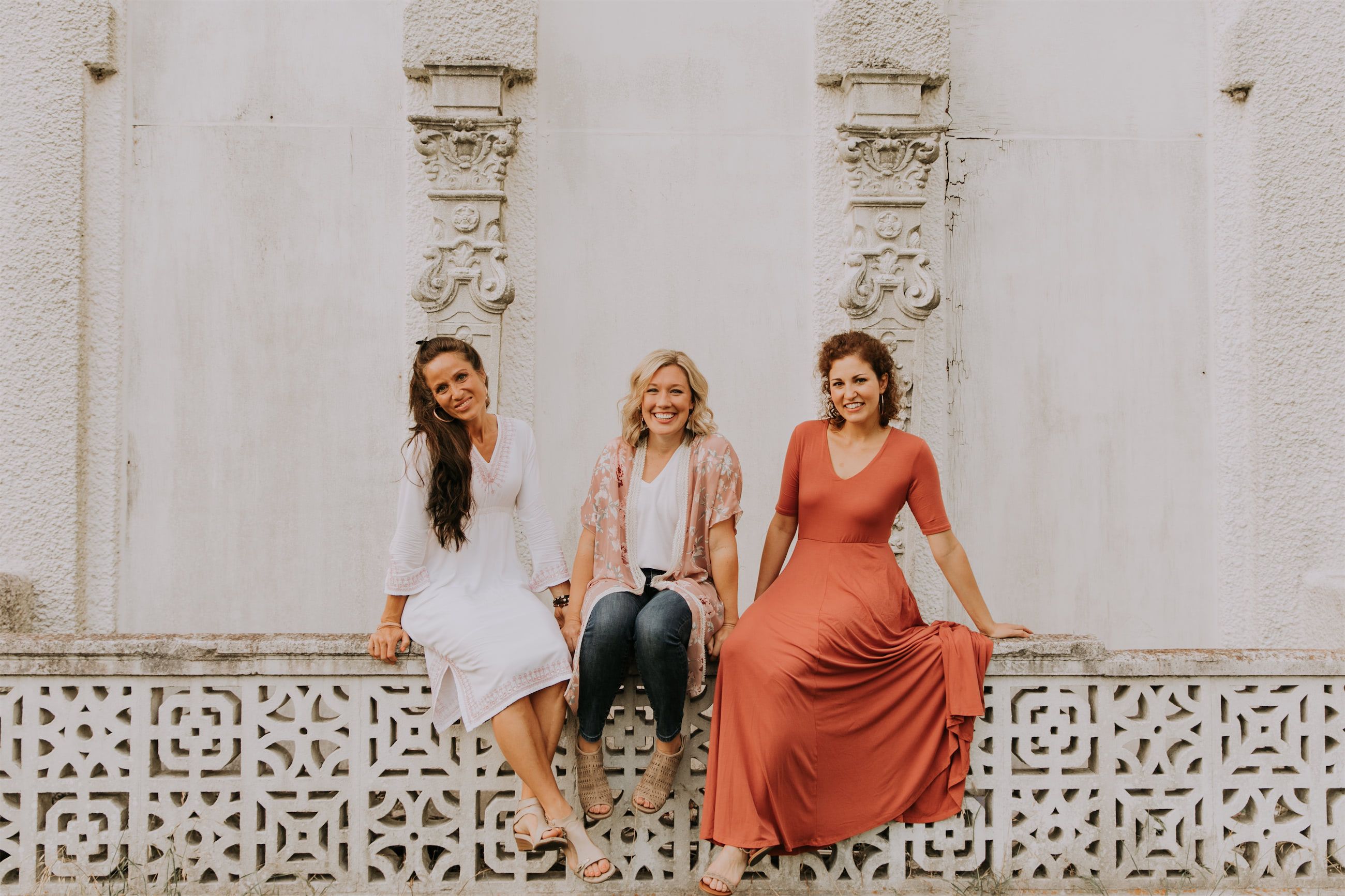 Kara Klein Oubre in a red dress, Christine Simpson Wessa in a flower shirt, and Maria Spears in a dress sitting on a stone wall version one