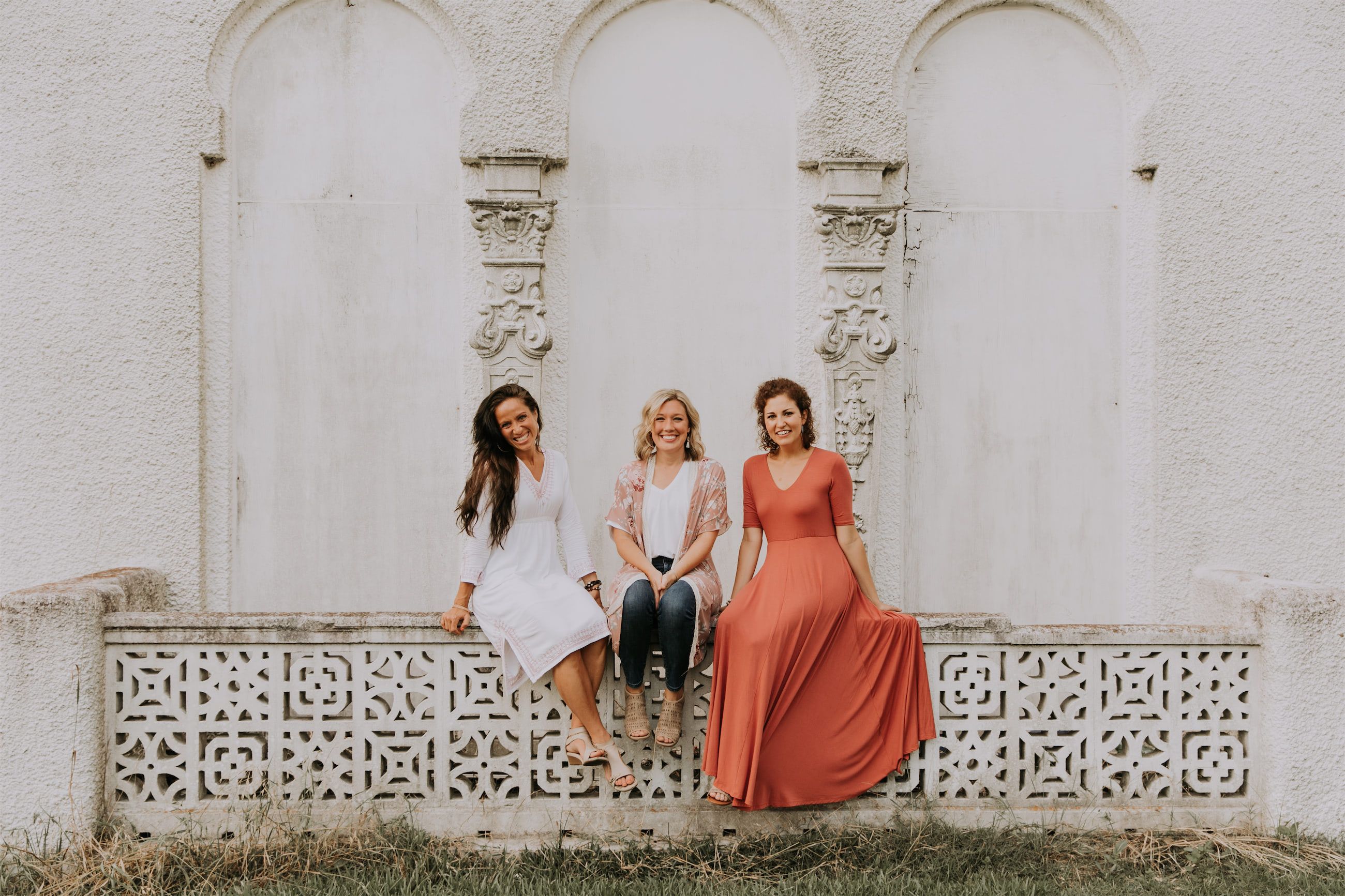 Kara Klein Oubre in a red dress, Christine Simpson Wessa in a flower shirt, and Maria Spears in a dress sitting on a stone wall version four