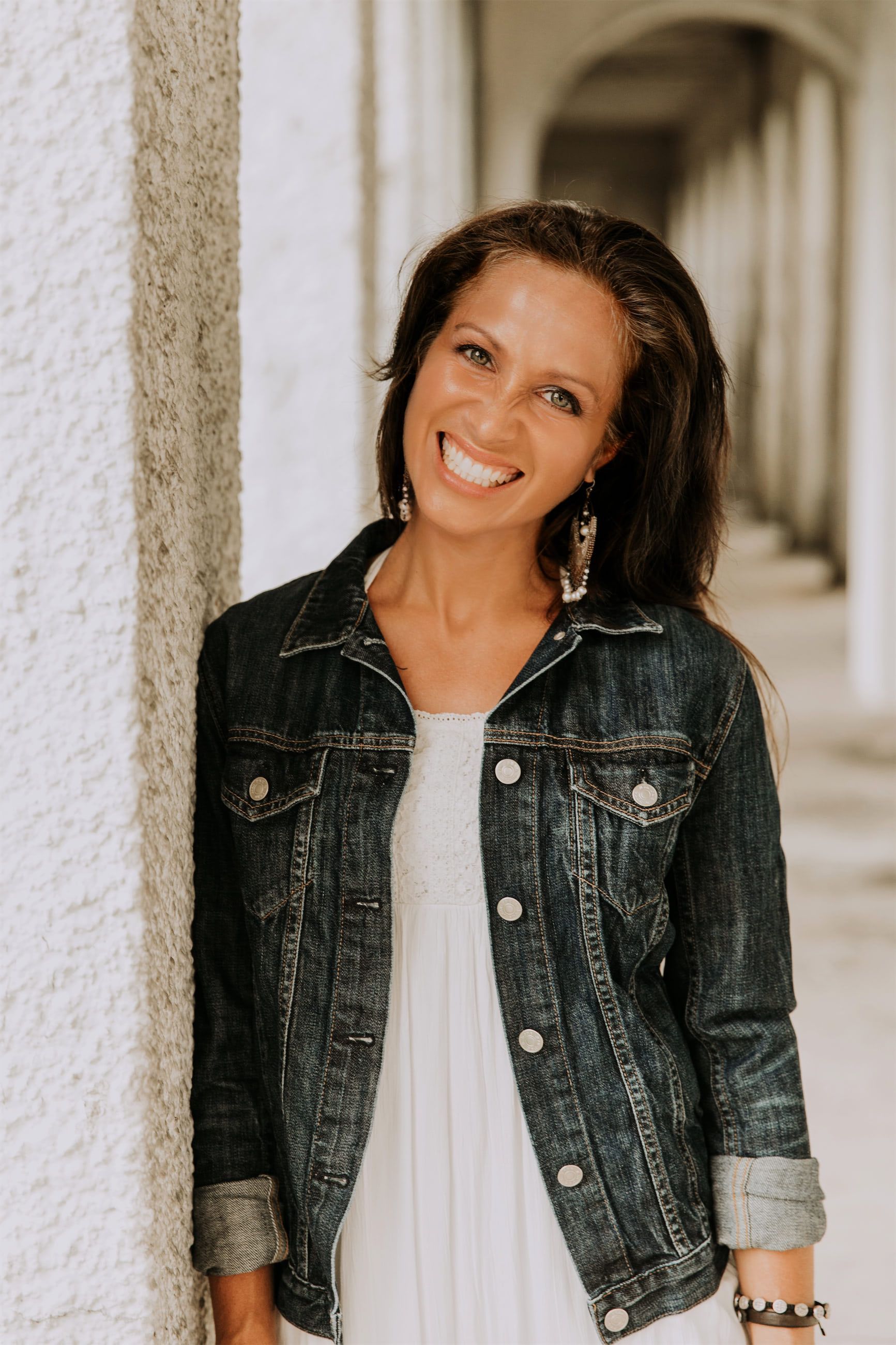 Maria Spears in a white shirt and jean jacket headshot by a white pillar version three
