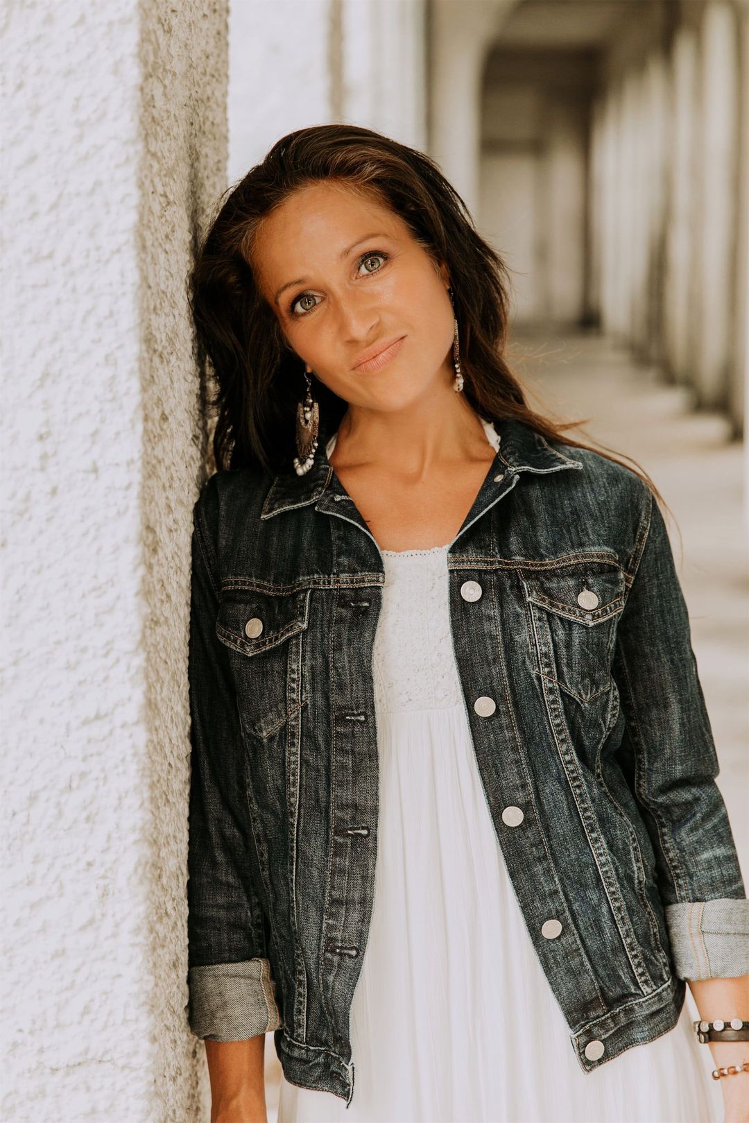 Maria Spears in a white shirt and jean jacket headshot by a white pillar version two
